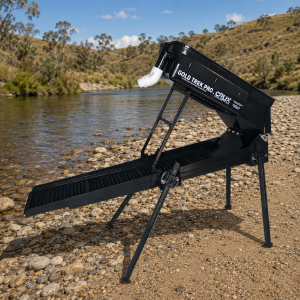 Black Gold Trek Pro CRUX Gen 5 backpack highbanker gold sluice on a rocky gravel bar beside a slow-flowing river and grassland.